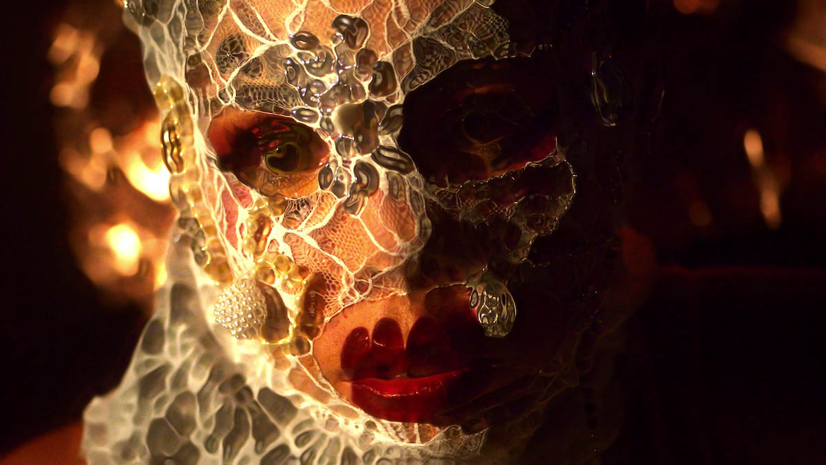 Close-up photo of the face of Sanni Est. It is covered with a white transparent laced mask. The mask is also partially covered with pearl pendants. The eyes and mouth remain uncovered. The black pupils and lipstick red mouth are distorted by image processing, and the face blurs outward. The right half of the face is in the shadow.